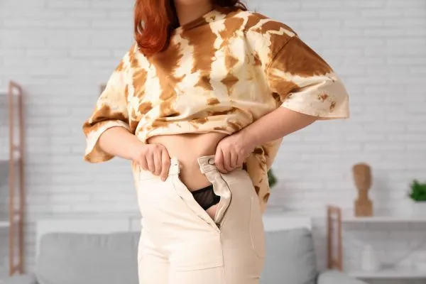Image of woman trying to do her trousers up after pregnancy weight gain Bournemouth